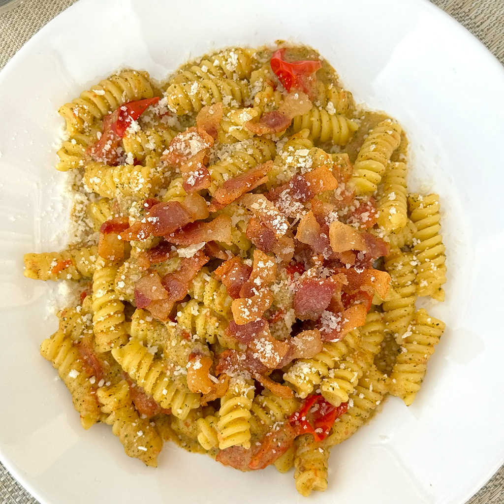 A plate of pasta with zucchini, cherry tomatoes, and guanciale from above