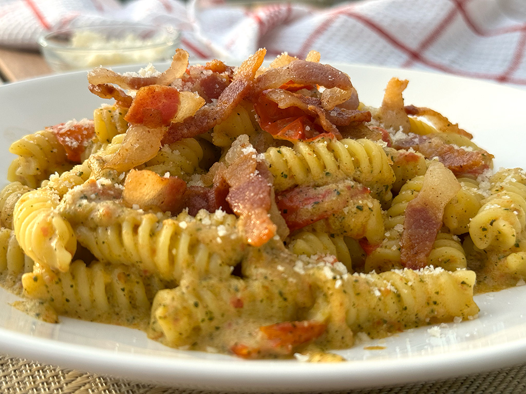 A closeup of pasta with zucchini, cherry tomatoes, and guanciale