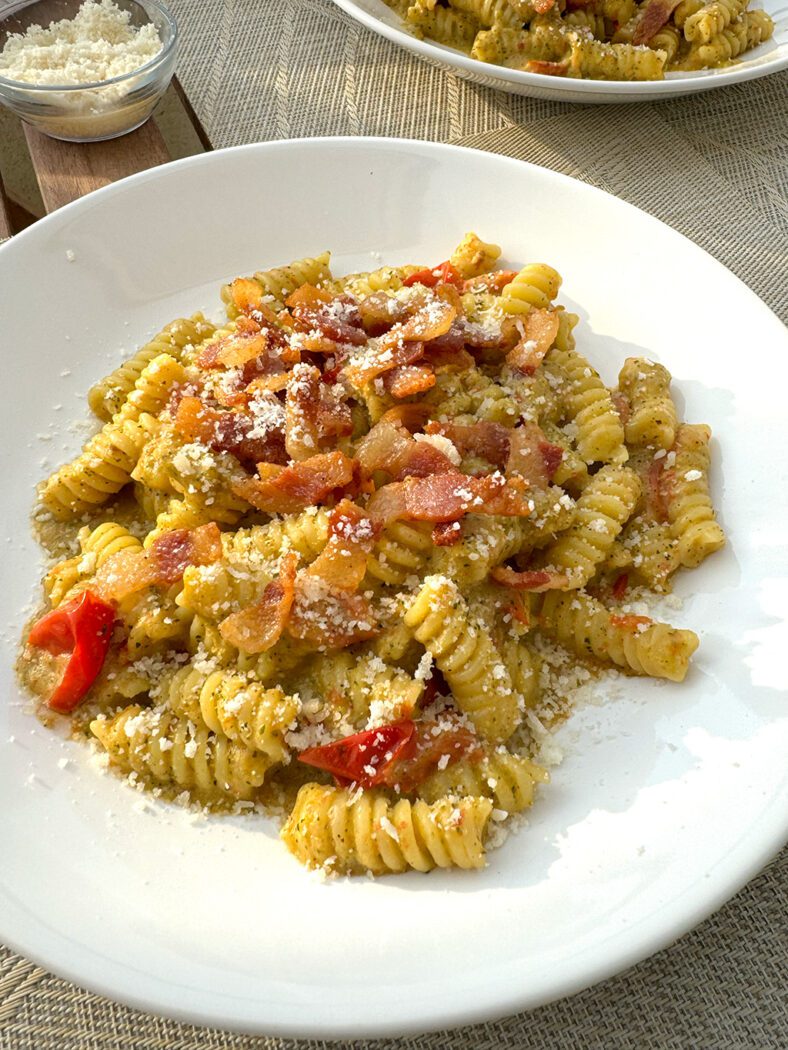 A plate of pasta on table with a bowl of grated cheese nearby